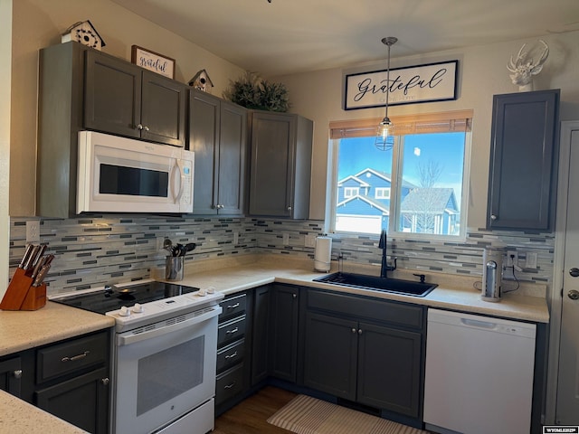 kitchen with decorative light fixtures, light countertops, decorative backsplash, a sink, and white appliances