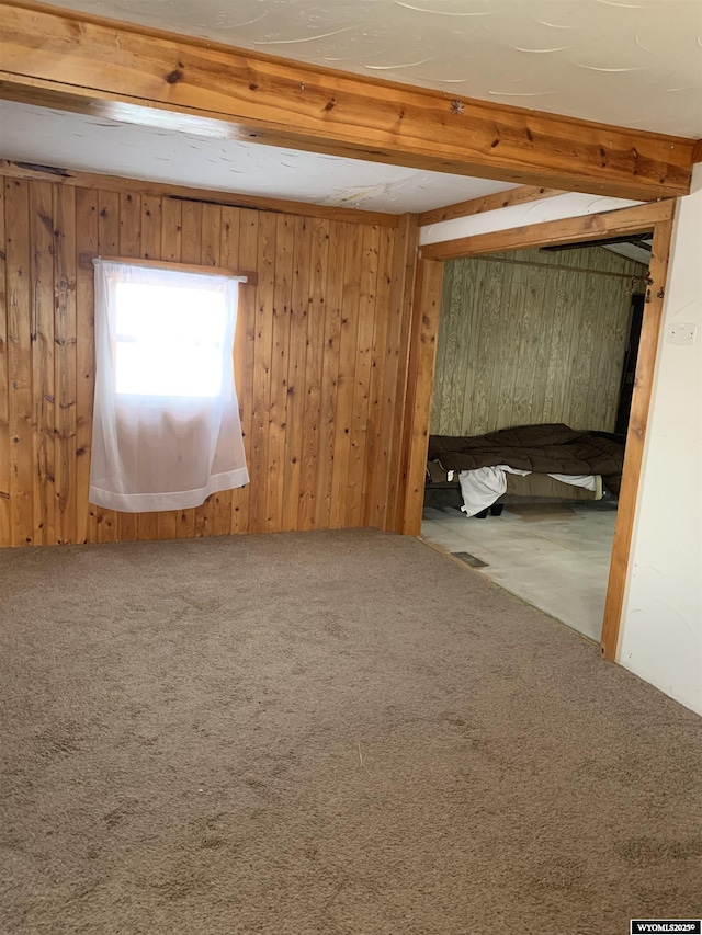 carpeted spare room featuring beamed ceiling and wooden walls