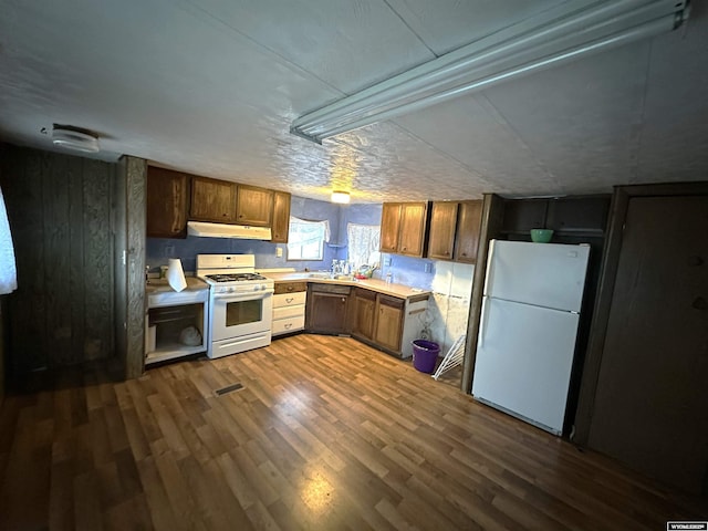 kitchen with light countertops, white appliances, dark wood finished floors, and under cabinet range hood