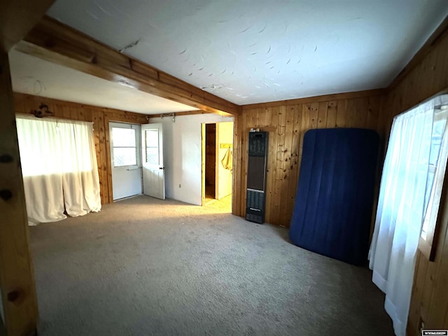 empty room featuring carpet, wooden walls, and beam ceiling