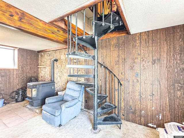 below grade area featuring stairs, a wood stove, wood walls, and a textured ceiling