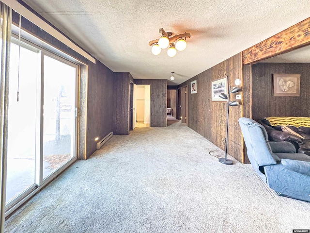 living area with a baseboard heating unit, carpet, wooden walls, and a textured ceiling