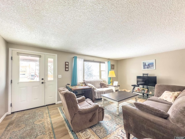 living room with light wood finished floors, a textured ceiling, and baseboards