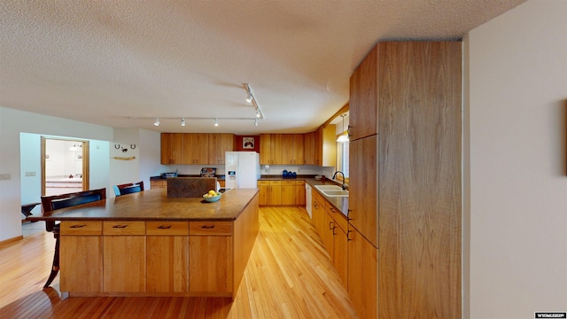 kitchen with white refrigerator with ice dispenser, a kitchen island, a sink, light wood-type flooring, and dark countertops