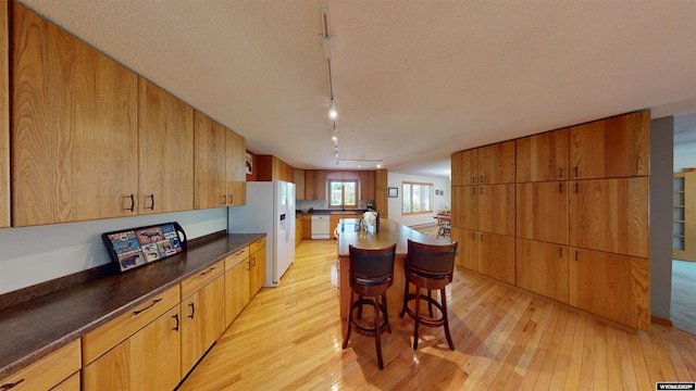 kitchen with dark countertops, white appliances, light wood-type flooring, and a center island