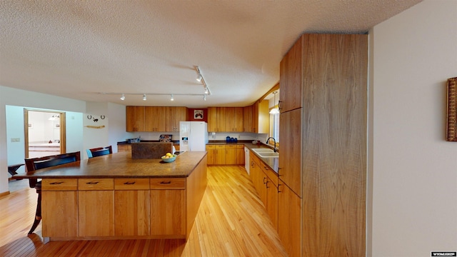 kitchen with dark countertops, light wood-style flooring, a center island, white fridge with ice dispenser, and a sink