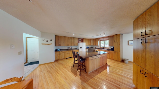 kitchen featuring a textured ceiling, a sink, light wood-type flooring, white fridge with ice dispenser, and dark countertops