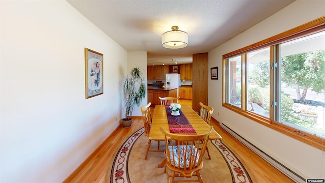 dining room with a baseboard heating unit, a healthy amount of sunlight, and light wood-style flooring