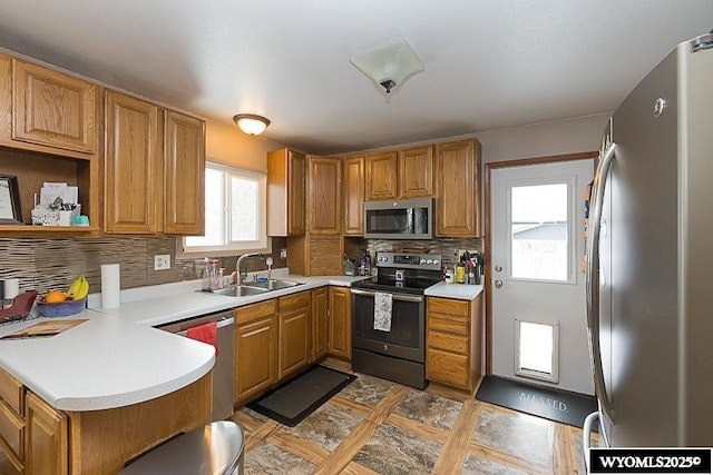 kitchen with appliances with stainless steel finishes, a peninsula, a sink, light countertops, and backsplash