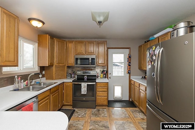 kitchen with stainless steel appliances, a sink, light countertops, backsplash, and brown cabinetry