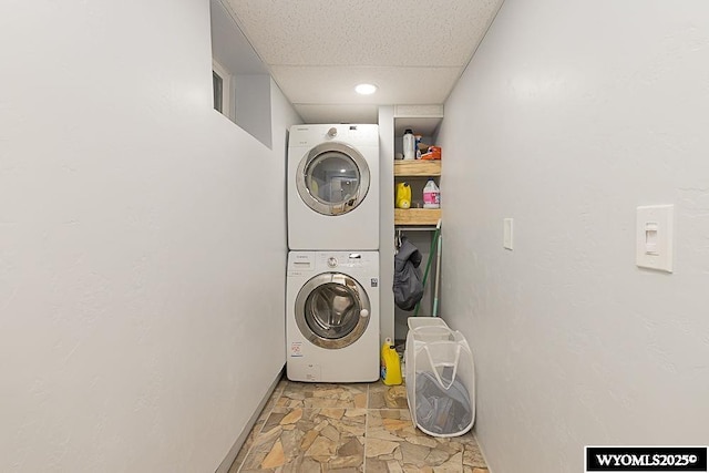 clothes washing area with laundry area, stacked washer and clothes dryer, stone finish floor, and baseboards