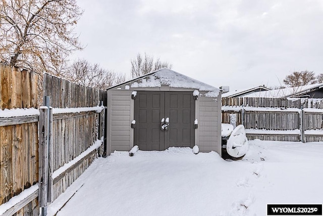 snow covered structure featuring an outbuilding, a fenced backyard, and a storage shed