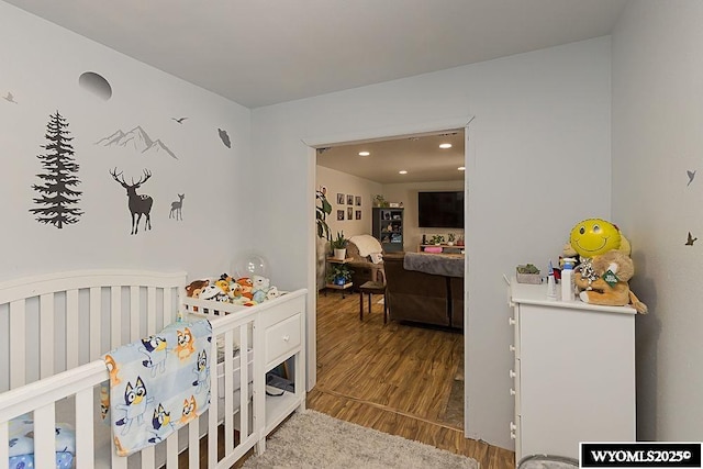 bedroom featuring recessed lighting, a crib, and wood finished floors