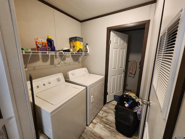 clothes washing area featuring laundry area, light wood finished floors, washer and clothes dryer, crown molding, and a textured ceiling