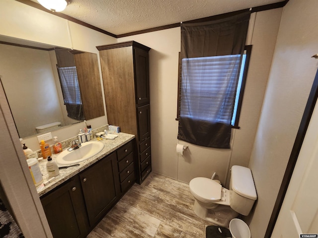 bathroom with toilet, ornamental molding, vanity, a textured ceiling, and wood finished floors