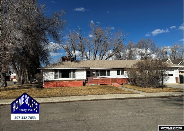 ranch-style home with a front lawn, driveway, a porch, a garage, and a chimney