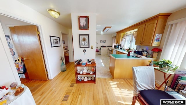 kitchen with brown cabinets, a peninsula, light wood-type flooring, and light countertops