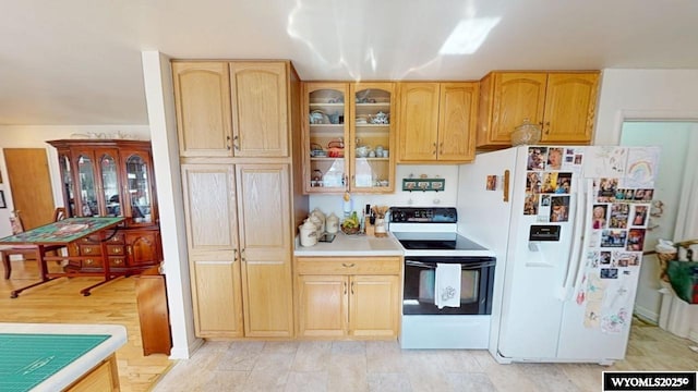 kitchen featuring glass insert cabinets, range with electric cooktop, white refrigerator with ice dispenser, and light countertops