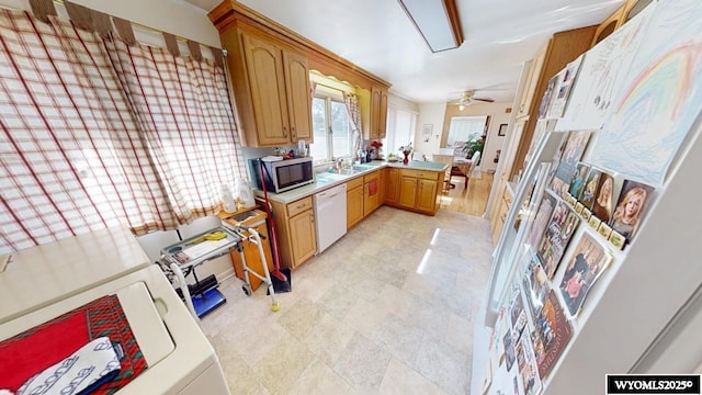 kitchen featuring stainless steel microwave, light countertops, washer / dryer, a peninsula, and white dishwasher