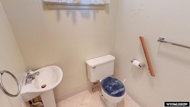 half bath featuring tile patterned floors, baseboards, toilet, and a sink