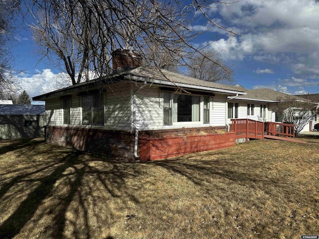 view of side of home featuring a lawn, a deck, and a chimney