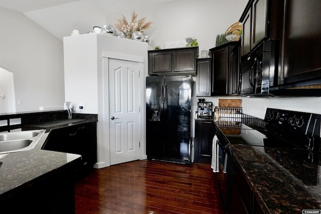 kitchen featuring dark stone counters, dark wood finished floors, vaulted ceiling, black appliances, and a sink