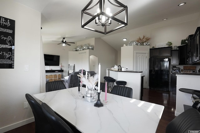 dining space featuring arched walkways, dark wood finished floors, vaulted ceiling, baseboards, and ceiling fan with notable chandelier