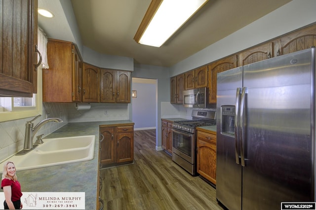 kitchen featuring appliances with stainless steel finishes, wood finished floors, a sink, and tasteful backsplash