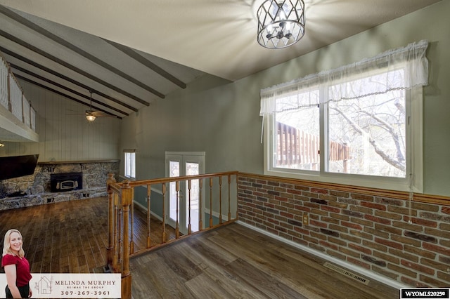 stairway with visible vents, lofted ceiling with beams, brick wall, wood finished floors, and a stone fireplace