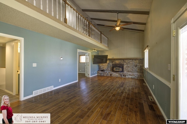 unfurnished living room with a towering ceiling, visible vents, hardwood / wood-style floors, and beamed ceiling