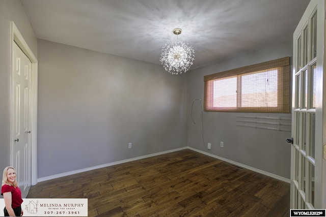 empty room featuring a notable chandelier, baseboards, and dark wood-style flooring