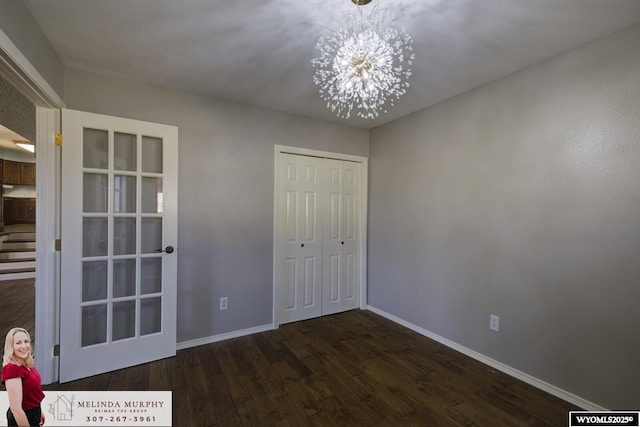 unfurnished bedroom with a chandelier, a closet, wood finished floors, and baseboards