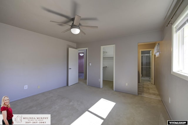 unfurnished bedroom with a spacious closet, a closet, carpet, and a ceiling fan