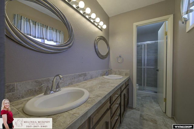 bathroom featuring double vanity, a sink, toilet, and a shower stall