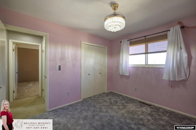 unfurnished bedroom featuring baseboards, a closet, carpet flooring, and a notable chandelier