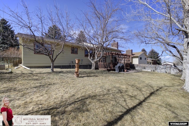 back of house featuring a lawn, a chimney, fence, and a wooden deck