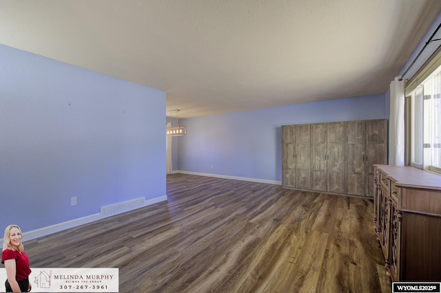 unfurnished living room with an inviting chandelier, baseboards, visible vents, and wood finished floors