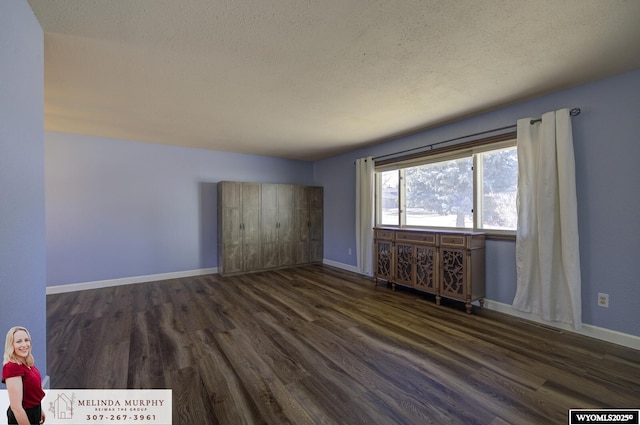 interior space featuring a textured ceiling, dark wood-type flooring, and baseboards