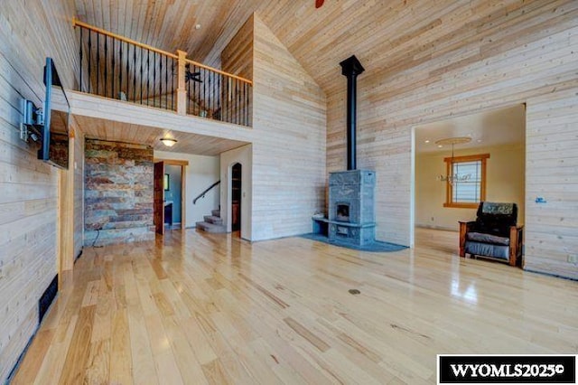 unfurnished living room featuring wooden ceiling, wood finished floors, a wood stove, stairs, and high vaulted ceiling