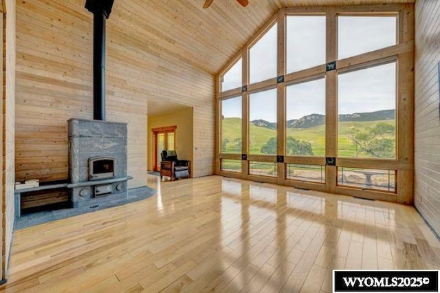 unfurnished living room with wooden ceiling, ceiling fan, wood finished floors, a wood stove, and high vaulted ceiling