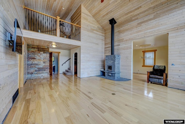 unfurnished living room featuring high vaulted ceiling, wooden ceiling, wood finished floors, stairs, and a wood stove