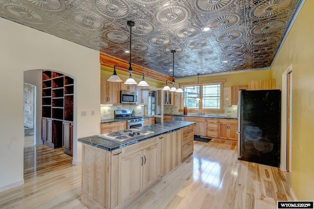 kitchen with arched walkways, dark countertops, an ornate ceiling, appliances with stainless steel finishes, and light brown cabinetry