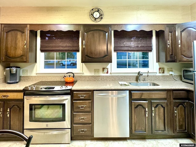 kitchen with dark brown cabinets, stainless steel appliances, a sink, and light countertops