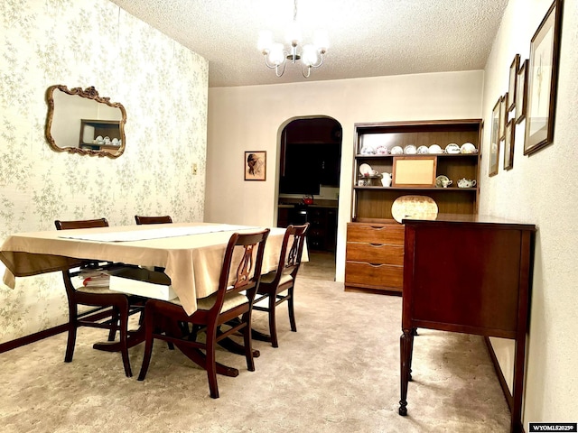 dining space featuring light carpet, wallpapered walls, arched walkways, a textured ceiling, and a notable chandelier