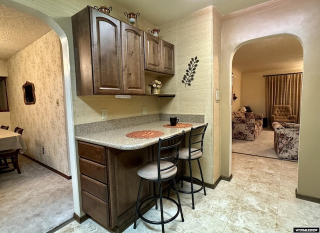 kitchen with arched walkways, light countertops, dark brown cabinetry, and baseboards