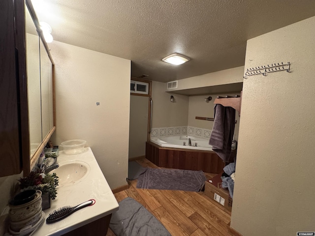 bathroom with double vanity, visible vents, a bath, wood finished floors, and a sink