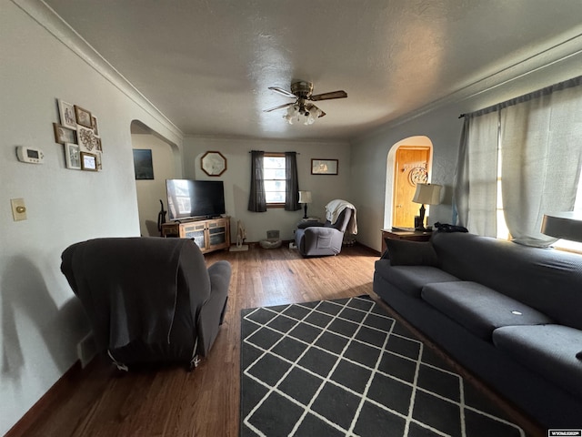 living room featuring ornamental molding, arched walkways, a ceiling fan, and wood finished floors