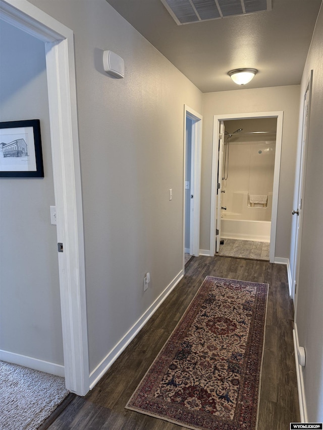 corridor featuring visible vents, baseboards, and wood finished floors