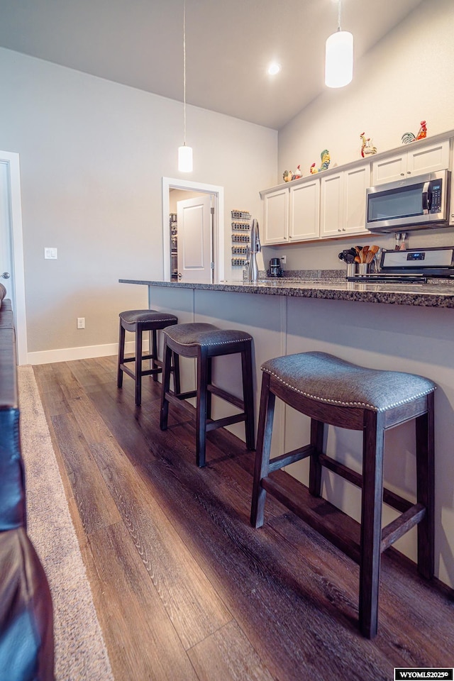 kitchen with dark wood finished floors, appliances with stainless steel finishes, a kitchen breakfast bar, hanging light fixtures, and white cabinetry