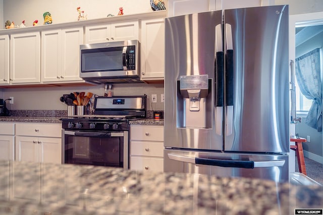 kitchen featuring stainless steel appliances, dark stone countertops, white cabinetry, and baseboards